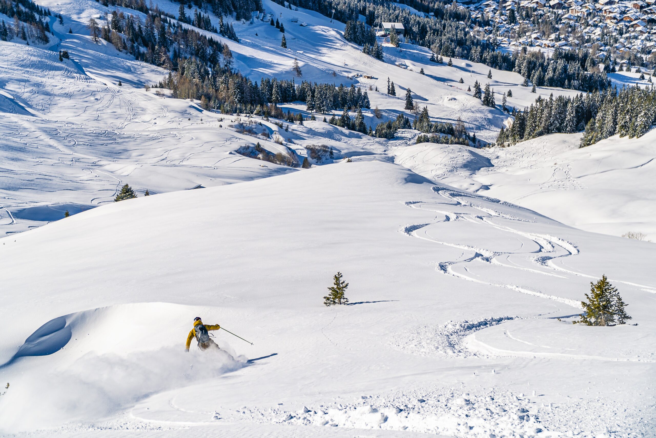 A high angle shot of a ski resort with ski tracks and a skier going down the slope